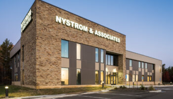 Exterior corner view of facility building with brick and metal cladding, entrance doors, and landscaping