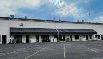 Exterior view of single-story white commercial building with black metal awning, parking lot, and clear sky