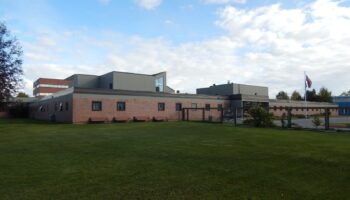 Exterior view of multi-section brick facility building with various architectural elements and grounds