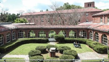 Exterior courtyard featuring brick arched colonnade, manicured hedges, green lawn, and arched windows