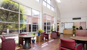 Interior lobby with burgundy seating, round tables, large windows with natural light, and wood flooring