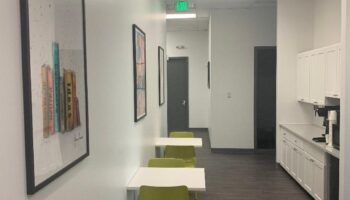 Interior hallway with white tables, green chairs, artwork, counter space, and modern cabinetry