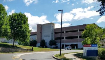 Exterior view showing emergency department entrance with parking garage, landscaping, and hospital directional signage