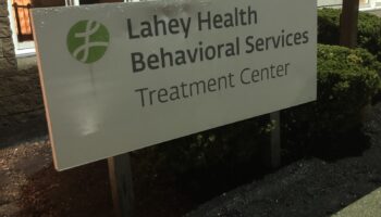 Exterior view of Lahey Health Behavioral Services Treatment Center sign with building entrance and windows in background
