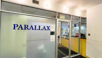 Interior main entrance showing frosted glass door with Parallax signage, reception area, and transparent glass partitions