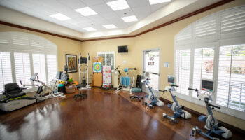 Interior fitness room with exercise bikes, treadmill, and therapy equipment on wooden flooring