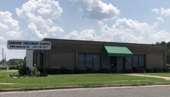 Exterior view of Sanford Treatment Center building with facility name sign, green awning, landscaping, and parking area