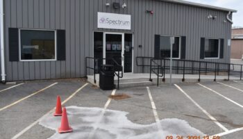 Exterior parking lot with marked spaces, facility entrance visible with metal railings and clear weather conditions