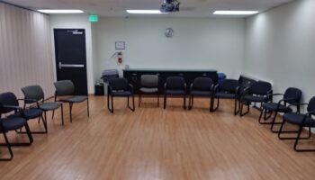 Interior large therapy space with rows of black chairs, wooden storage furniture, projector, and curtains
