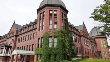 Exterior view of large historic red brick building with distinctive dome towers and ivy-covered walls