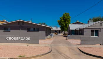 Exterior view of Crossroads treatment facility showing main entrance with signage, connected buildings, courtyard area, and clear Arizona sky