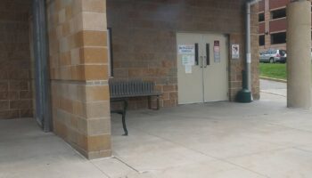 Exterior entrance area with brick facade, metal support columns, cream-colored double doors with ReDiscover Transitions signage, bench seating, and concrete walkway