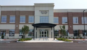 Exterior view of behavioral healthcare facility with brick and stone facade, covered entrance, and landscaped grounds