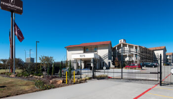 Exterior entrance with decorative iron gate, facility signage displaying 1075 address, and multi-story residential building structure