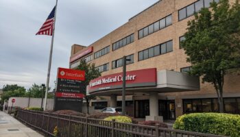 Exterior view of Interfaith Medical Center main entrance with brick building, red signage, landscaping, and parking area