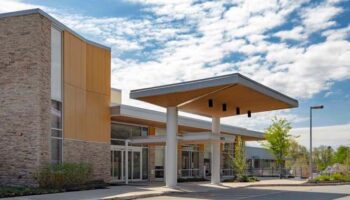 Exterior view of modern rehabilitation hospital entrance with brick and metal facade, covered portico, and landscaping