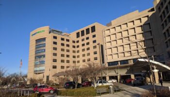 Exterior view of Mercy Health St. Rita's Medical Center with tan brick facade, main entrance, landscaping, and visitor parking area