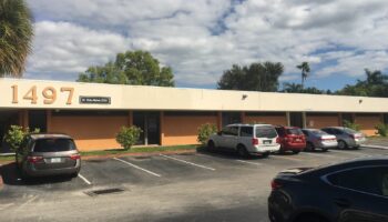 Exterior front view of treatment center building with address 1497, tan facade, parking area with multiple vehicles, and landscaping