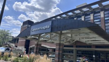 Exterior view of Evanston Hospital main entrance showing signage, covered portico with modern architecture, landscaping, and parking area