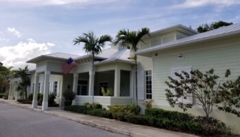 Exterior front entrance of treatment facility showing white building with covered entry portico, American flag, and landscaping