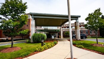 Exterior view of hospital entrance with covered canopy, landscaped grounds, and sidewalk approach