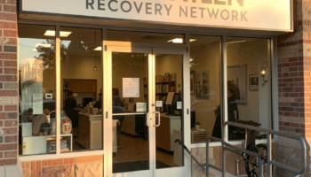 Exterior storefront entrance of Ten Sixteen Recovery Network showing illuminated sign, glass doors, brick facade, and entry ramp