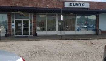 Exterior front entrance of treatment center showing brick facade, glass doors, windows, and SLMTC sign with parking area