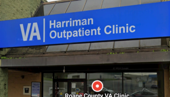 Exterior view of Roane County VA Clinic entrance featuring blue VA Harriman Outpatient Clinic sign, glass doors, and brick facade