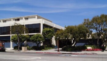 Exterior view of modern multi-story treatment center building with white facade, large windows, landscaping, and street frontage