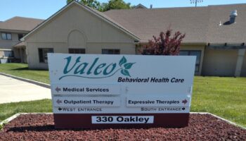 Exterior directional signage for Valeo Behavioral Health Care showing medical services and therapy entrances with facility building visible