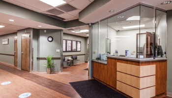 Interior lobby with wooden reception desk, glass partitions, waiting seating, and professional healthcare facility design