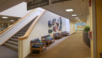 Interior hallway featuring stairs with wooden railings, directional signs for Ob/Gyn and Physical Therapy, and seating areas