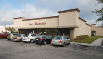 Exterior commercial building with PAR Services signage, beige and brown facade, parking spaces with vehicles
