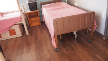 Interior bedroom with two beds with pink linens, wooden nightstands, chair, and hardwood floor