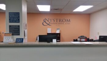 Interior reception area with Nystrom & Associates branding on orange accent wall, front desk counter with staff workspace