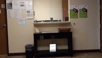 Interior reception area with check-in desk, informational postings on walls, and waiting area with seating