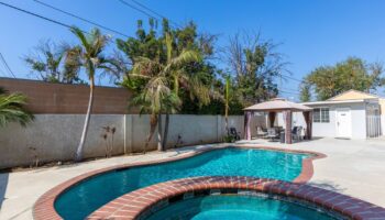 Exterior view of swimming pool with spa, lounge seating, and landscaped grounds surrounded by walls