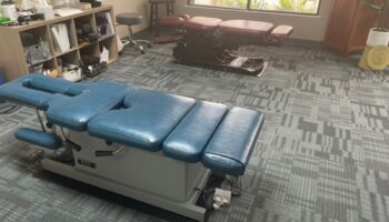 Interior treatment room featuring medical equipment with blue and burgundy padding and storage shelving along walls