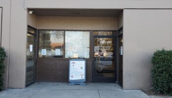 Exterior storefront of BAART Programs showing main entrance with facility signage, dark framed door, informational postings, and landscaping