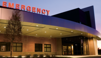 Exterior emergency department with red signage, brick facade, covered canopy, and evening lighting.