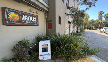 Exterior view of Janus of Santa Cruz building with neon sign, landscaping, and parking area visible