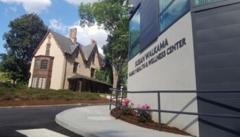 Exterior view of historic white building adjacent to modern dark medical facility with signage and landscaping