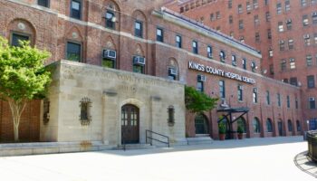 Exterior stone and brick building with arched entrance and Kings County Hospital Center signage visible from plaza.