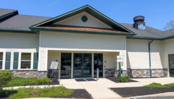 Exterior front entrance of treatment facility with white siding, stone base, green trim, entrance pavilion with glass doors, and landscaping