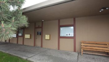 Exterior front entrance of treatment facility with tan building, burgundy trim, palm tree landscaping, and concrete walkway