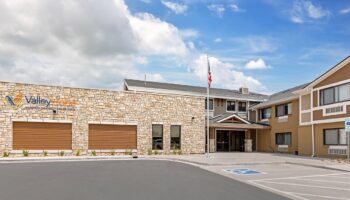 Exterior front entrance of Valley Hope treatment center showing stone facade, Valley Hope signage, main entrance doors, and parking area with American flag