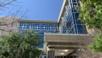 Exterior view of modern medical facility with blue-glass windows, brick construction, main entrance canopy, and landscaping.