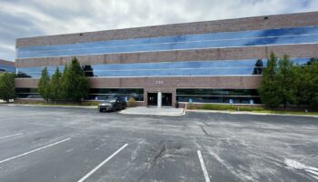 Exterior of treatment center showing main entrance, parking lot, brick and glass facade with blue window panels, and landscaping