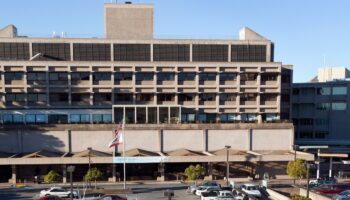 Exterior of treatment facility showing multi-story concrete building with horizontal window bands, ground-level entrance canopy, and parking area.
