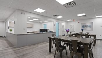 Interior reception desk and open dining area with tables, modern furnishings, and bright overhead lighting